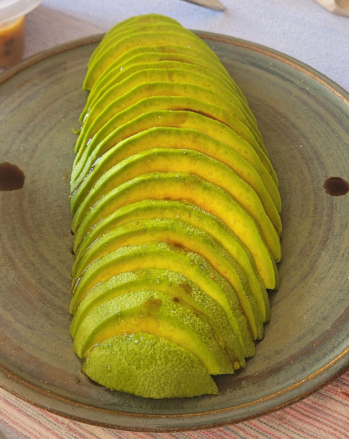 Un aguacate rebanado y abierto en abanico sobre un plato de barro.