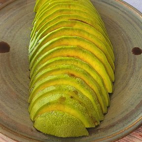 Un aguacate rebanado y abierto en abanico sobre un plato de barro.