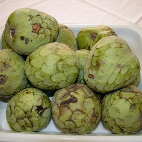 Chirimoyas apiladas en un platón blanco, con la piel escamosa a la vista.