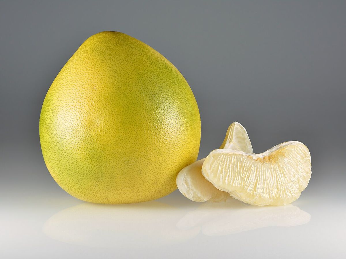 Pomelo amarillo entero junto a dos gajos pelados, sobre fondo gris.
