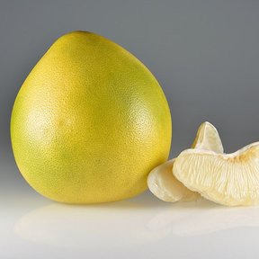 Pomelo amarillo entero junto a dos gajos pelados, sobre fondo gris.