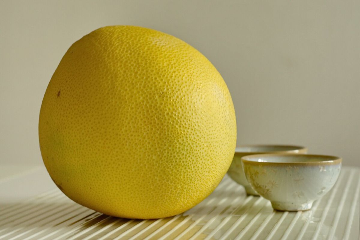 Pomelo amarillo junto a dos tazones de barro, sobre un mantel de rayas.