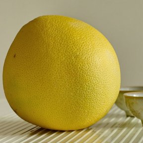 Pomelo amarillo junto a dos tazones de barro, sobre un mantel de rayas.