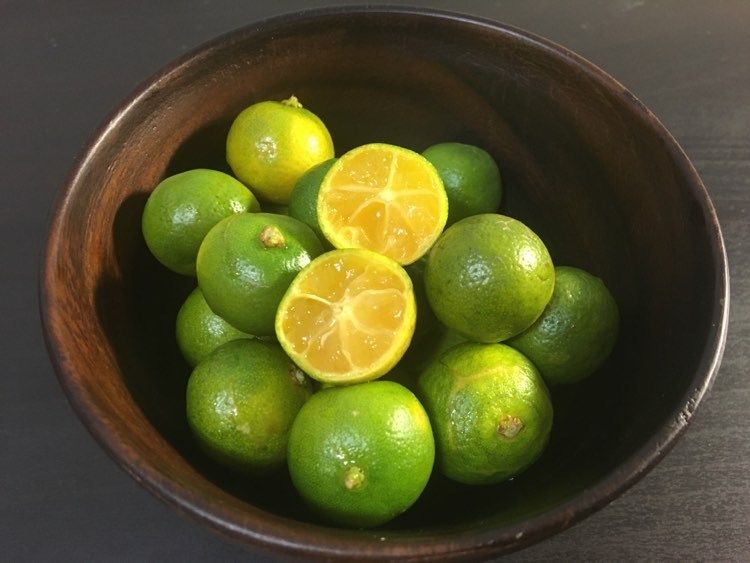 Frutos verdes en un tazón de madera, uno partido a la mitad.