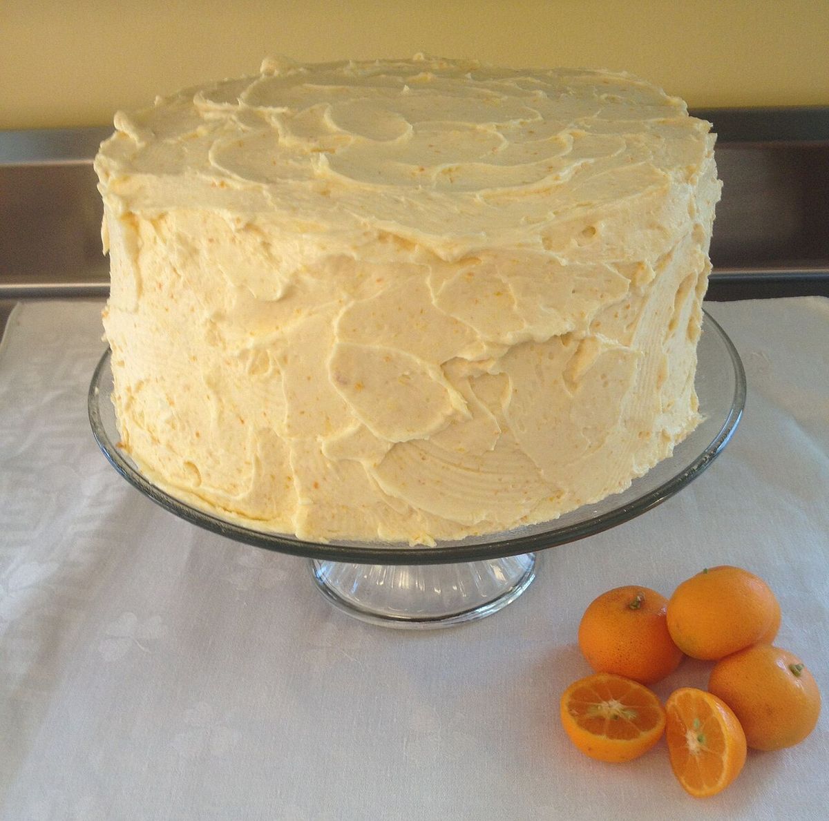 Un pastel cubierto de betún junto a unos frutos cítricos sobre un mantel.