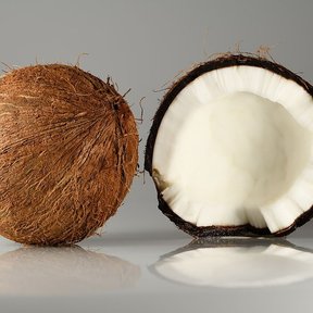 Un coco entero y otro partido a la mitad, sobre un fondo gris de estudio.