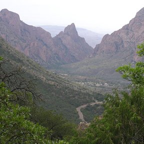Cañón entre farallones rojizos con un valle boscoso al fondo.