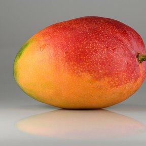 Un mango maduro, rojo y amarillo, fotografiado sobre un fondo gris.