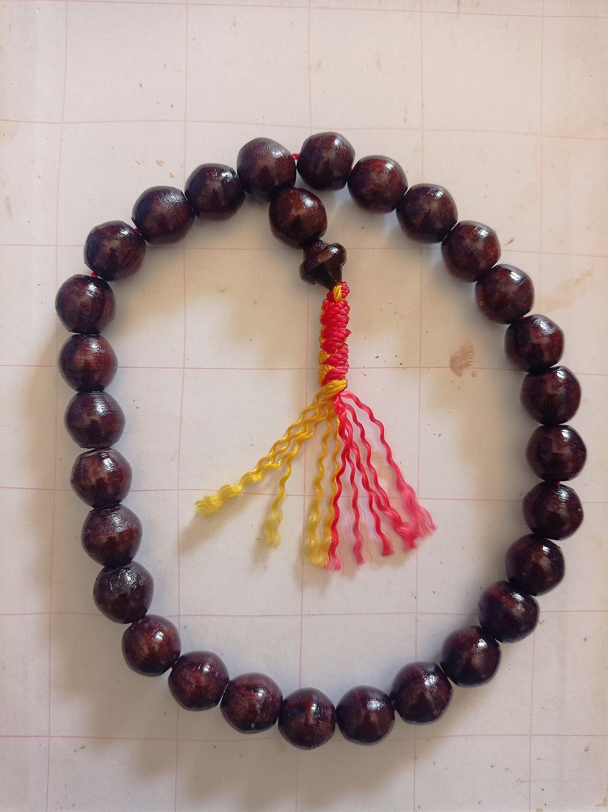 Pulsera de cuentas redondas y oscuras de madera de paraíso, con una borla de hilo.