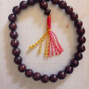 Pulsera de cuentas redondas y oscuras de madera de paraíso, con una borla de hilo.