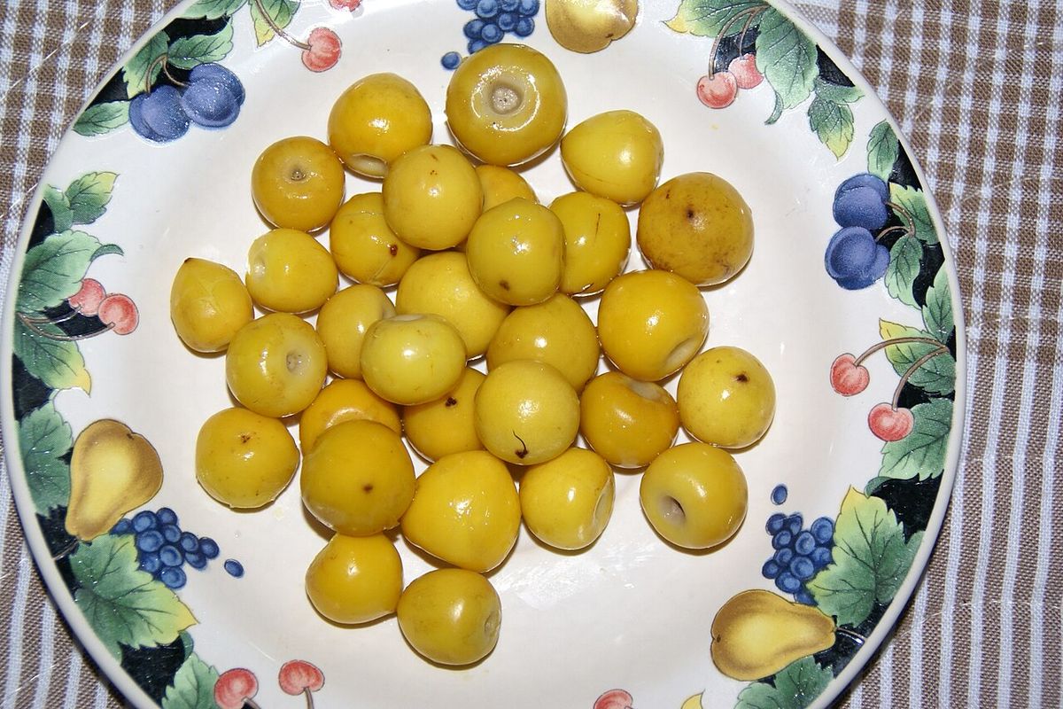 Nanches amarillos amontonados en un plato de loza floreada sobre un mantel.