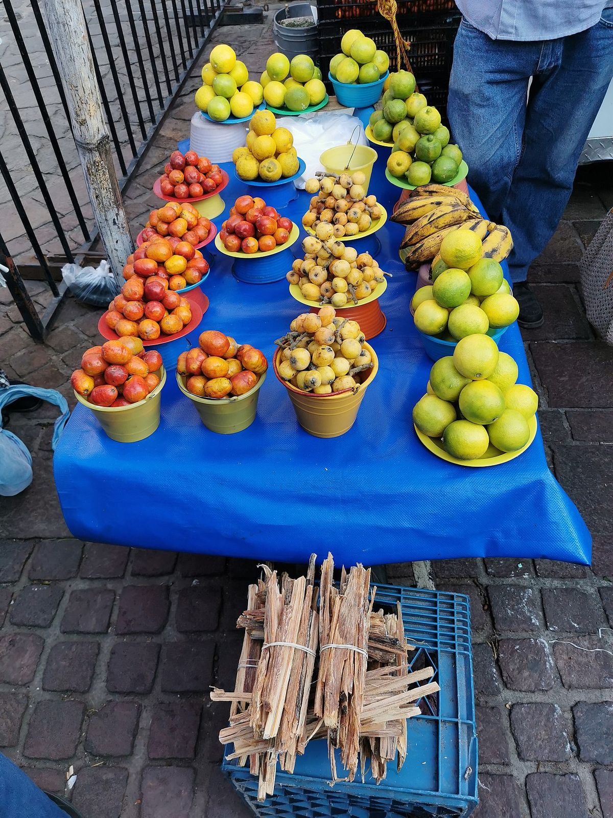Puesto de fruta en la calle con rajas de ocote apiladas en el suelo.